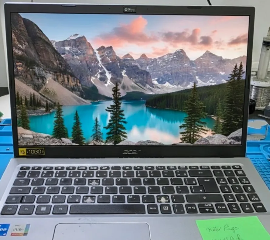 Acer Aspire 3 A315-58 aberto na bancada com a tela mostrando um papel de parede de lago e montanhas e um bilhete adesivo verde sobre a base