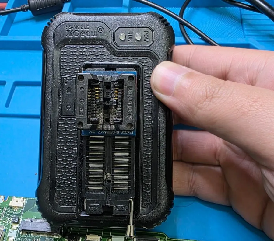 Programador de memórias XGecu com um adaptador de soquete SOP8, segurado pela mão do técnico