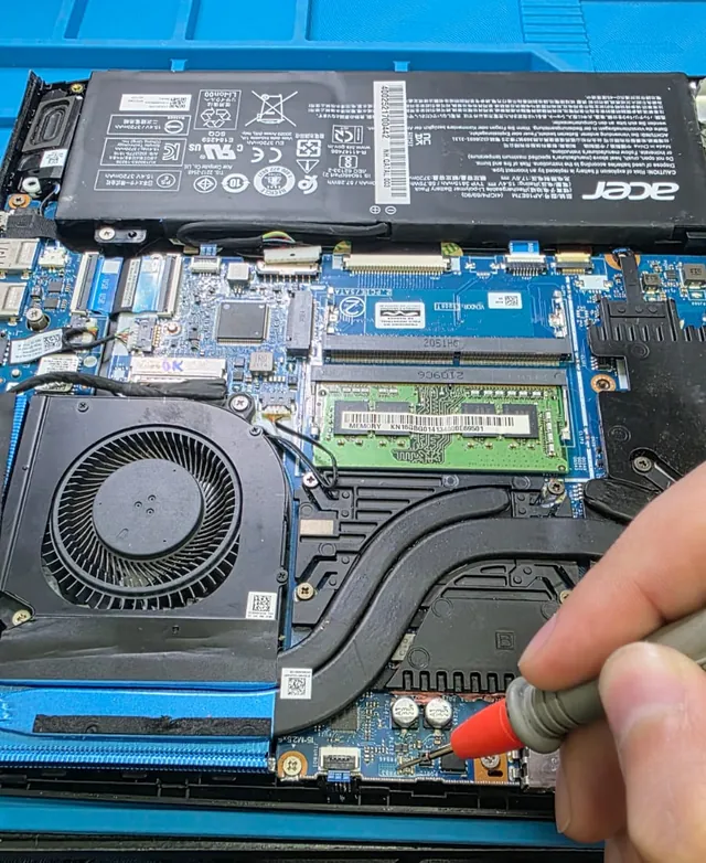 Acer Predator Helios 300 aberto na bancada, com a ponta de prova do multímetro medindo a placa-mãe ao lado do dissipador