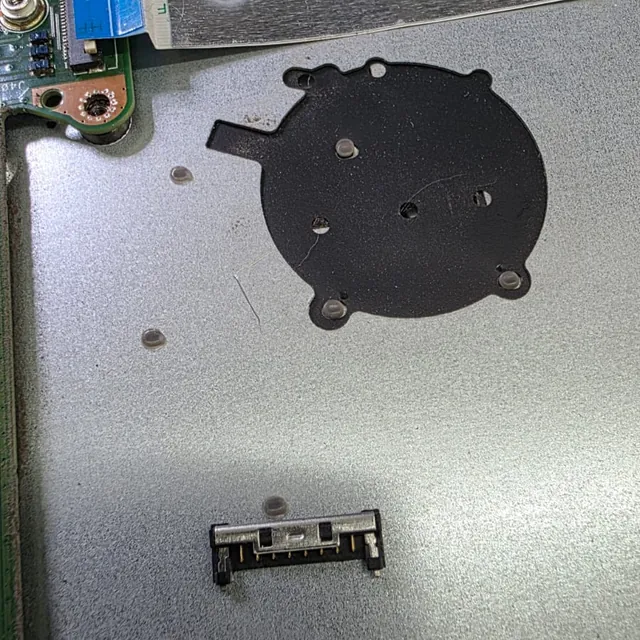 Conector da bateria de um ASUS X515J solto sobre a carcaça metálica do notebook, ao lado do anteparo preto do ventilador