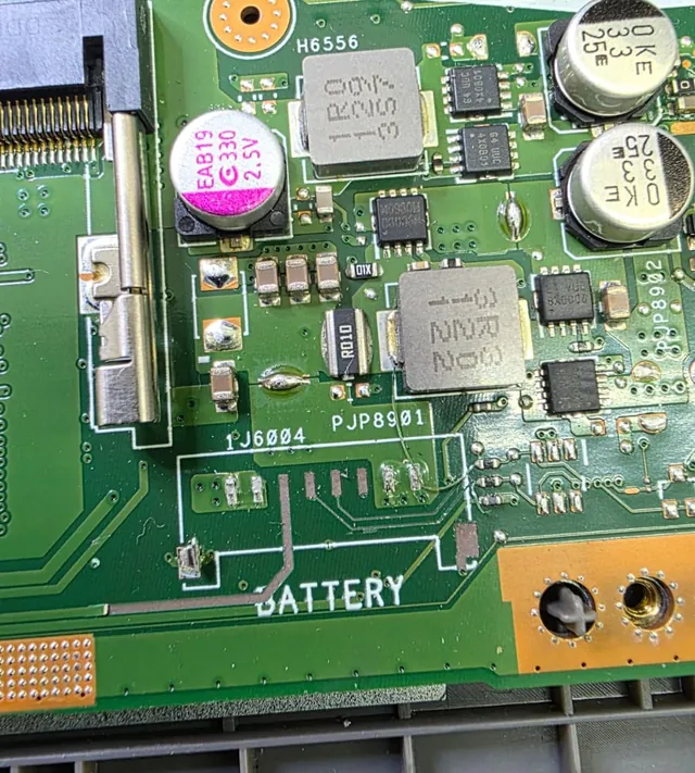 Placa-mãe de ASUS X515J na região marcada BATTERY, com as ilhas de cobre expostas onde o conector foi arrancado