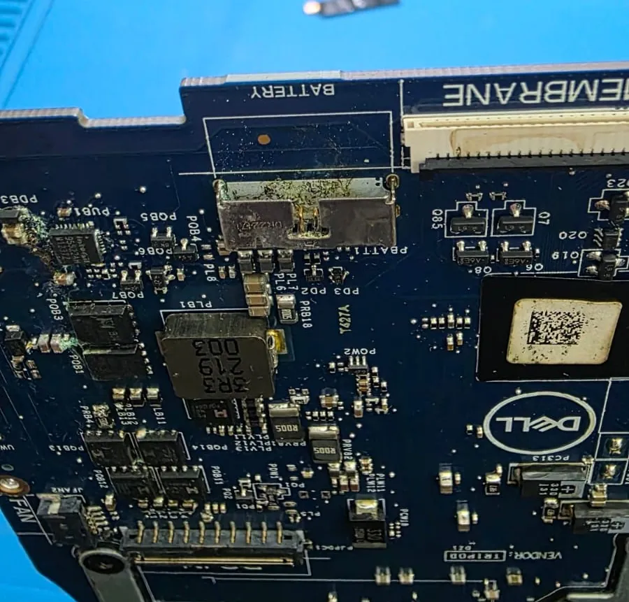 Placa-mãe de um Dell G15 5525 vista de perto, com resíduo escuro e oxidação em volta do conector da bateria e dos componentes vizinhos