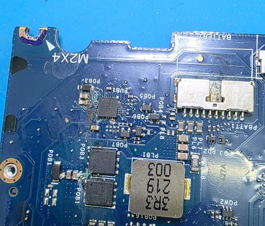 Placa-mãe do Dell G15 5525 mostrando resíduo esverdeado ao lado de CIs e transistores, perto da marcação M2X4 e do conector da bateria