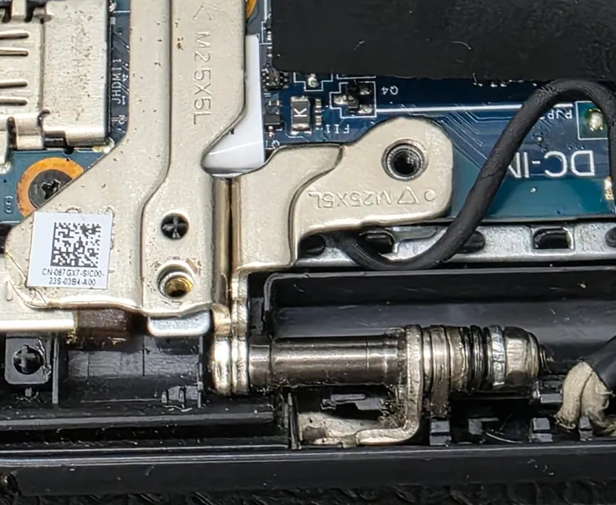 Dobradiça metálica do Dell Inspiron 3511 vista por dentro, ao lado da região da placa com a serigrafia DC-IN
