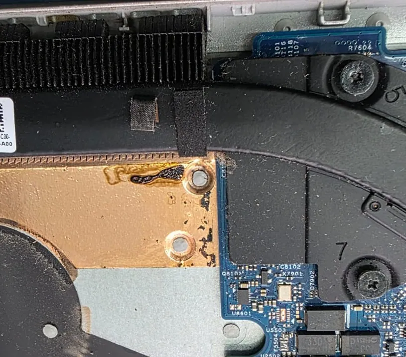 Interior do Dell Inspiron 5584 com o dissipador de calor e a ventoinha cobertos de poeira e uma placa de cobre com resíduo escuro perto de um parafuso