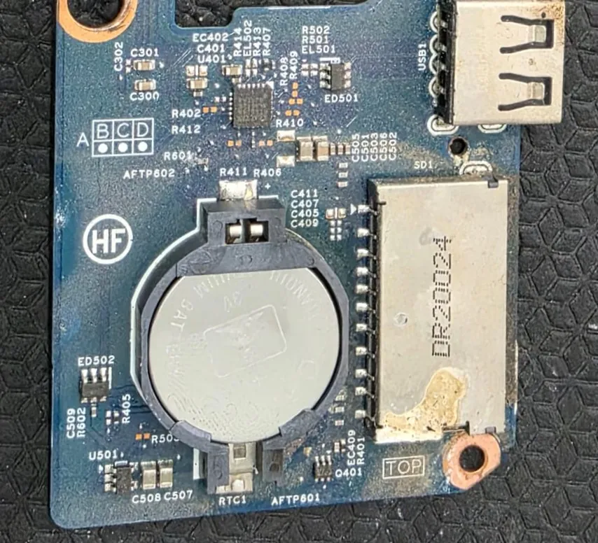 Placa filha do Dell Inspiron 5584 com a bateria do relógio, o leitor de cartão SD e a porta USB, com resíduo esbranquiçado e manchas de oxidação em volta do leitor
