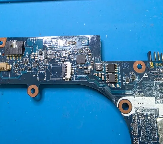 Região da placa-mãe do Dell Inspiron 7520 entre o conector de energia e o conector da bateria, com resíduo de fluxo de solda