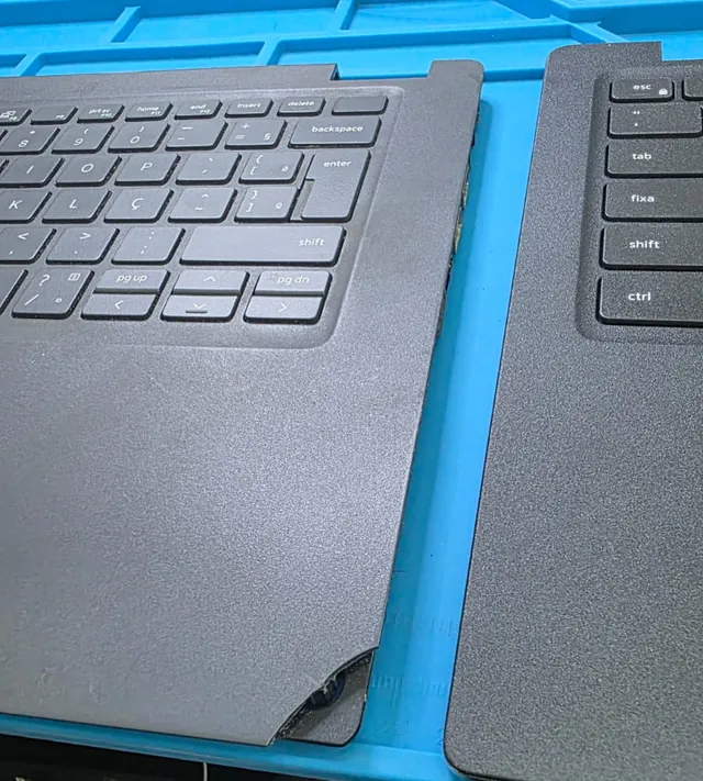 Palmrest do Dell Latitude 3520 retirado do notebook, com o canto quebrado ao lado de outra peça do teclado