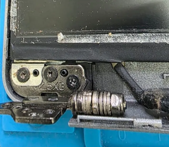 Dobradiça de um Dell Latitude 5420 vista com a base aberta, com os parafusos de fixação e a gravação M25X3 na peça