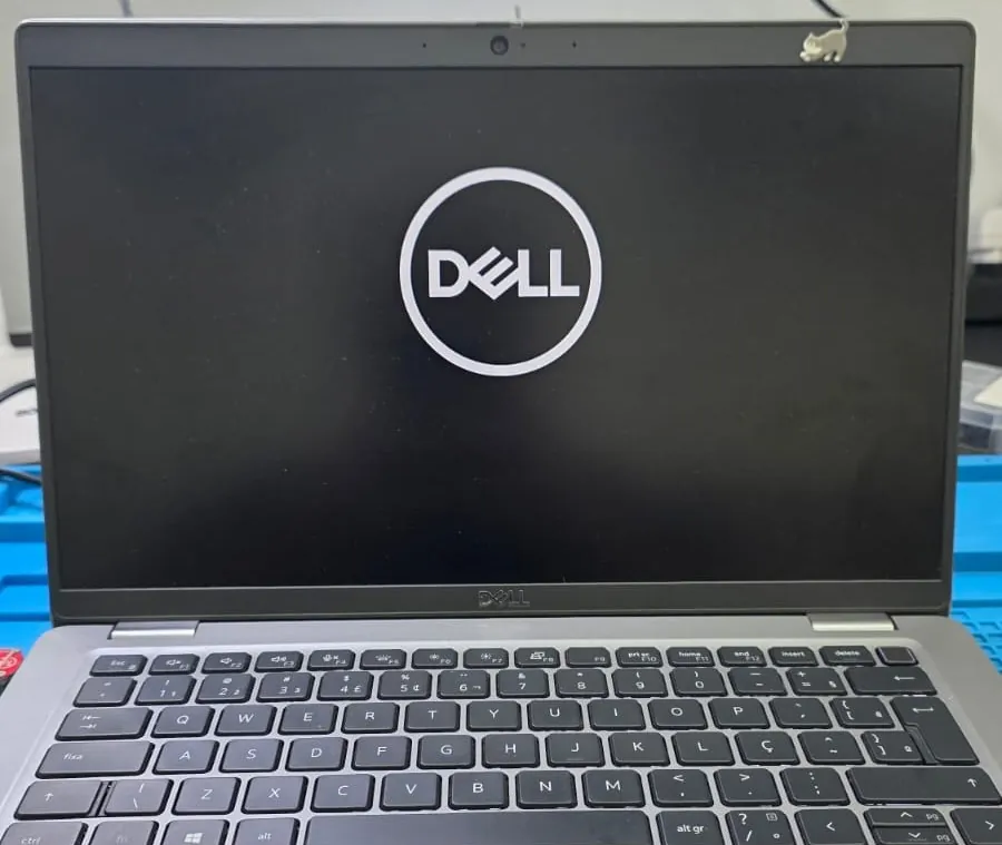 Dell Latitude 5420 ligado na bancada, com a tela mostrando o logotipo da Dell, o teclado à frente e a dobradiça ao fundo