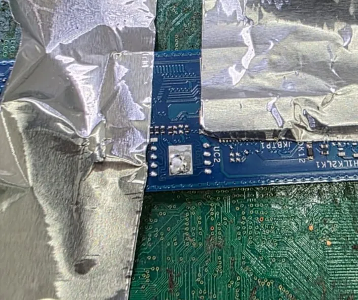 Região da placa do Latitude 5450 protegida com fita de alumínio, com o espaço vazio e estanhado do chip de BIOS, marcado UC2, depois de ele ser retirado