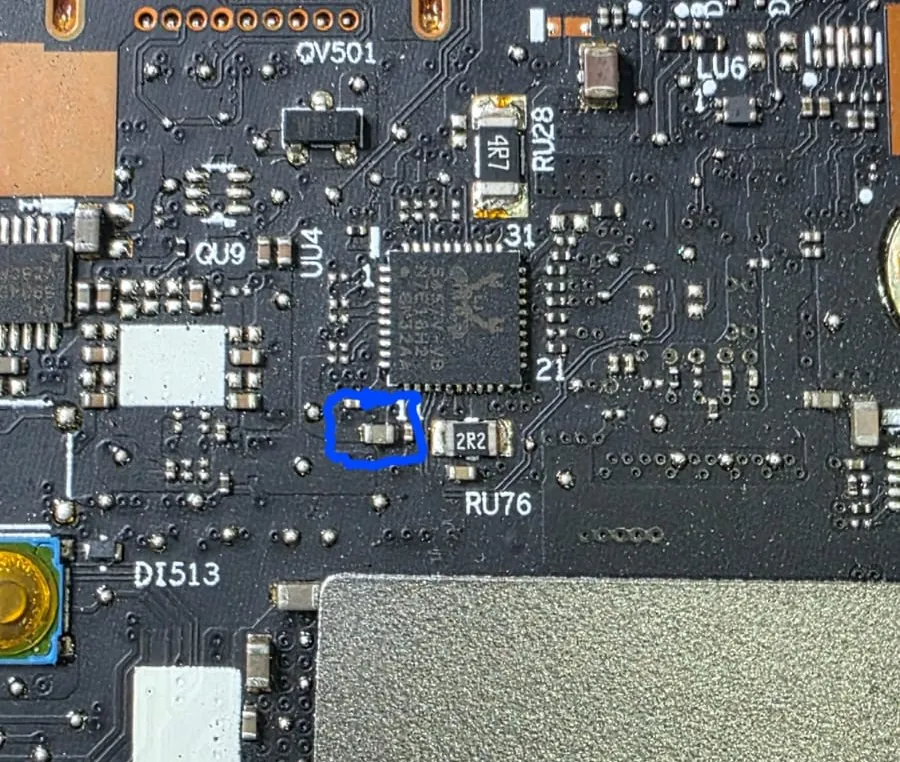 Região da placa-mãe do Lenovo Legion Pro 7 com o componente trocado marcado em azul, ao lado de um circuito integrado e de um resistor de 2R2