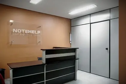 Recepção da Notehelp na Vila Mariana, com a placa de vidro da marca na parede e o balcão de atendimento